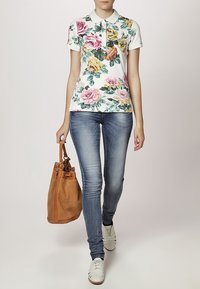 Polo shirt floral avec des roses roses et jaunes sur un fond blanc, associé à un jean skinny bleu clair et un sac à main en daim beige.