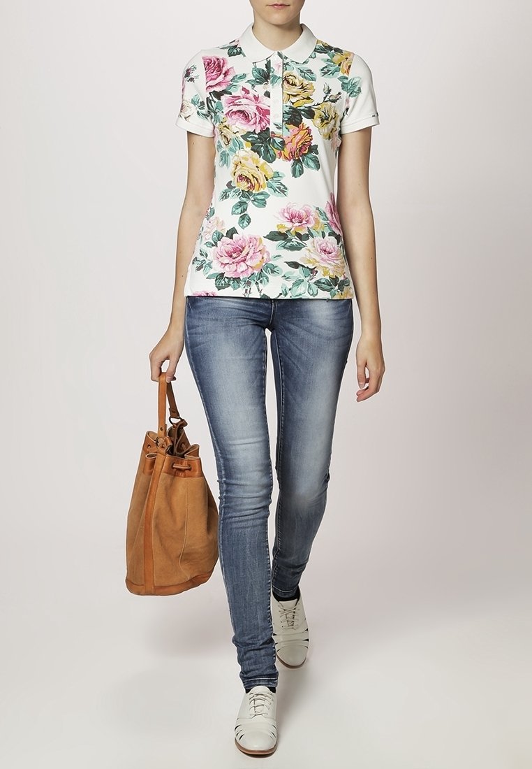 Polo shirt floral avec des roses roses et jaunes sur un fond blanc, associé à un jean skinny bleu clair et un sac à main en daim beige.