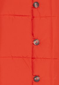 Lys orange quiltet stof med synlig horisontal syning og tre mørke marmorerede knapper, der er justeret lodret.
