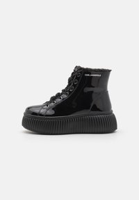 Zwarte gepatineerde leren enkelboots met een textured, gegroefde zool, voorzien van een bontkraag en vetersluiting. Het logo aan de zijkant is zichtbaar.