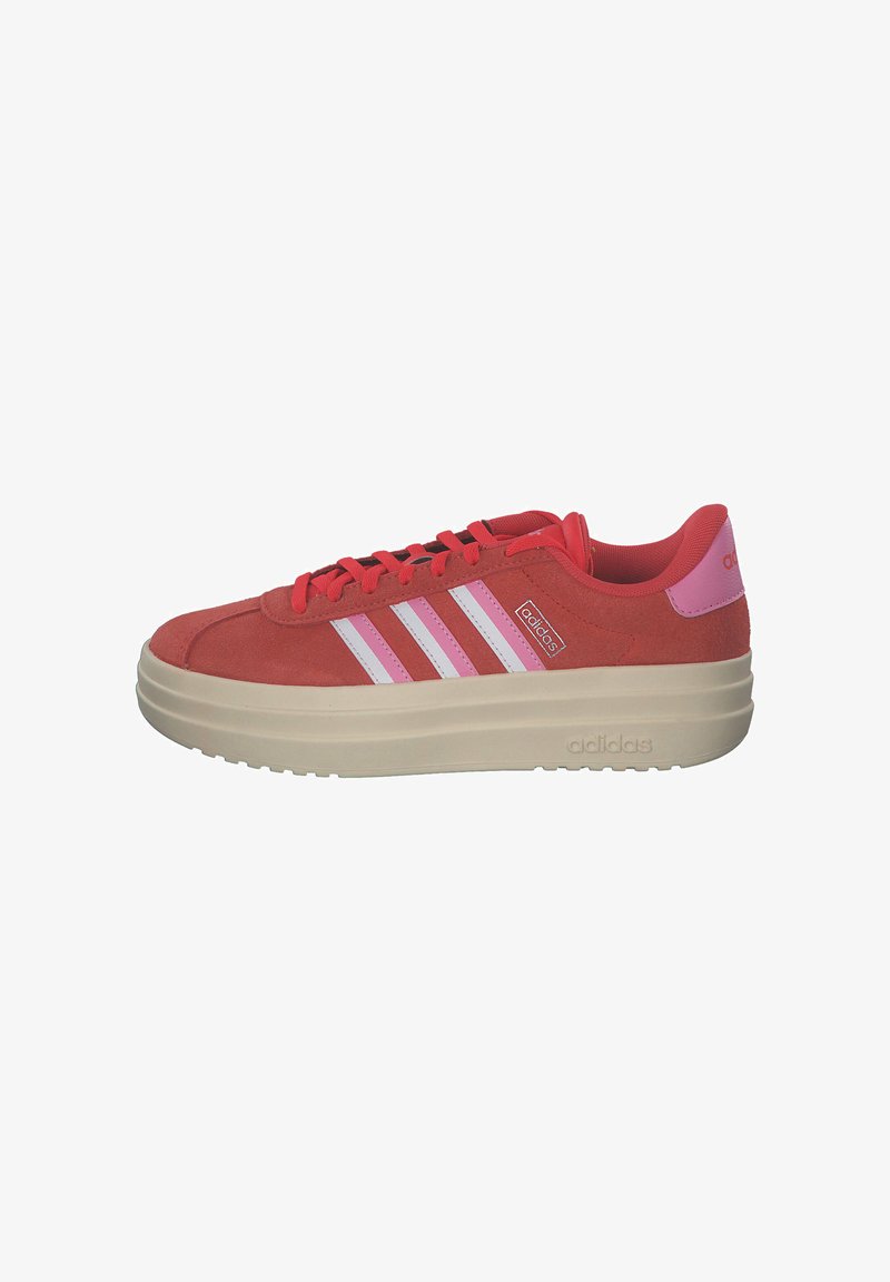 Crvene zamšaste tenisice s tri bijele pruge, okruglim vrhom i podstavljenim ovratnikom. Imaju debeli kremasti platforma potplat i prošivene detalje.