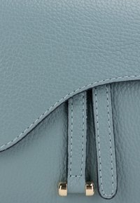 Hellblau strukturierte Ledertasche mit goldenen Beschlägen, die eine geschwungene Klappe und gestickte Riemenverzierungen aufweist.