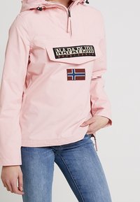 Jasnoróżowa, długorękawowa bluza z kapturem, z przednią kieszenią, naszywką z logo i akcentem w postaci norweskiej flagi. Gładka tekstura.