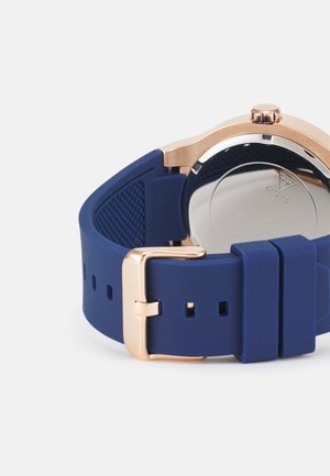 Plavi silikonski remen za sat s metalnim ružičastim zlatnim kopčanjem, s teksturiranim dizajnom duž remena i reflektirajućim stražnjim kućištem.