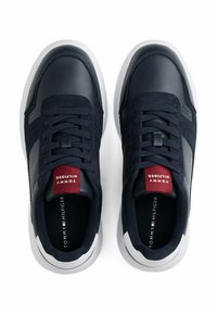 Un paio di sneakers blu navy e bianche con lacci neri, etichetta rossa sulla linguetta e il marchio "Tommy Hilfiger" sulla linguetta e sulle solette.