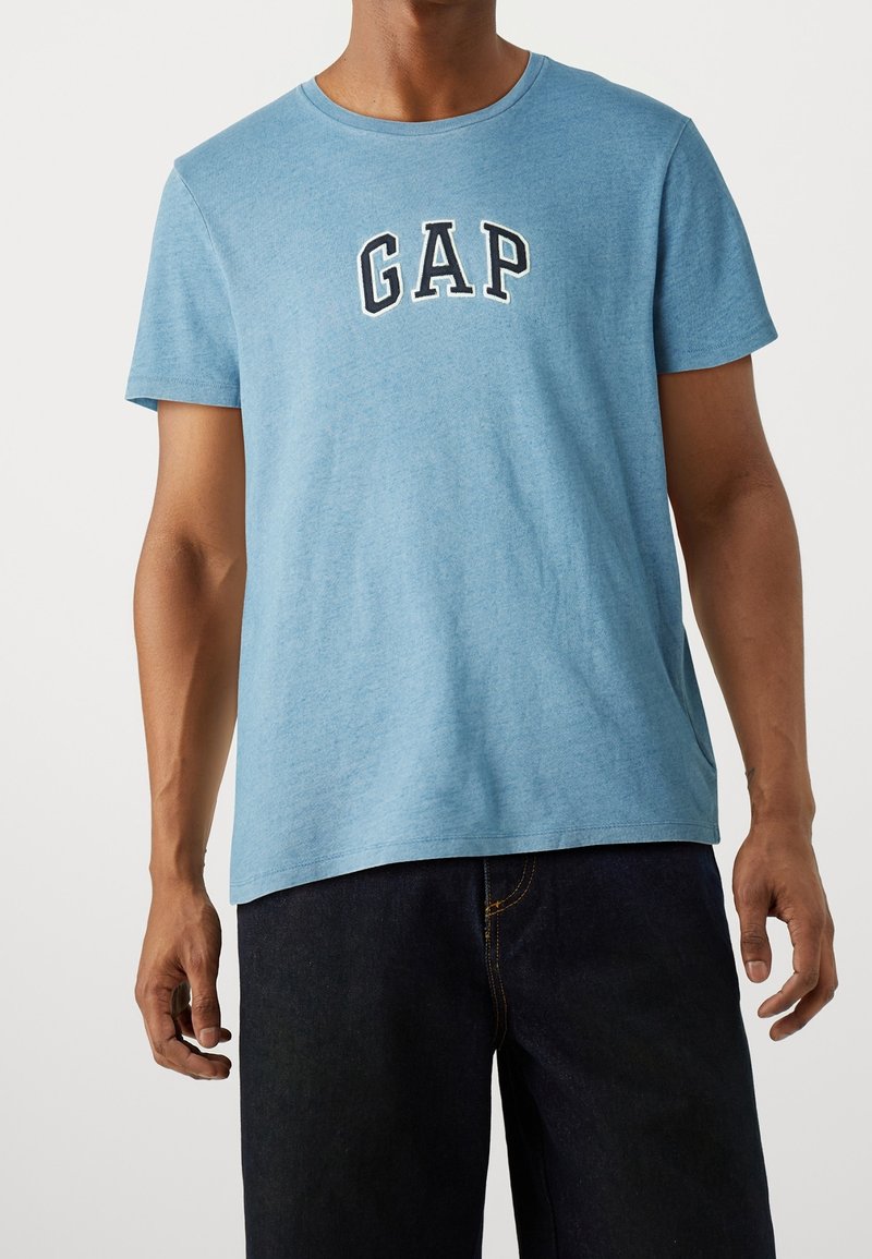 Helles blaues Baumwoll-T-Shirt mit Rundhals. Mit dem schwarzen, gestickten "GAP"-Logo auf der Brust. Lässiger Schnitt mit kurzen Ärmeln.
