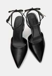 Scarpe con tacco alto nere con punta affusolata e cinturino alla caviglia. Realizzate in pelle liscia, con un dettaglio a fiocco sul cinturino.