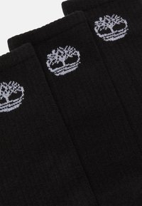 Calze di cotone nere con logo di un albero bianco, texture a coste e design di lunghezza media sopra il polpaccio. Presenta tre paia esposti insieme.