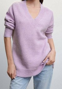 Pull violet clair à col en V avec manches courtes et poignets et ourlet côtelés. Fabriqué en matière douce et texturée. Porté sur un jean bleu clair.