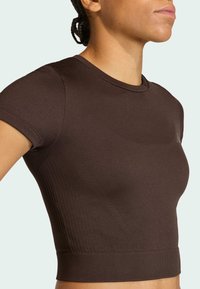 Καφέ ριμπ κοντομάνικη crop top με εφαρμοστή γραμμή, διαθέτει στρογγυλή λαιμόκοψη και διακριτική λεπτομέρεια με λογότυπο στο στήθο ς.