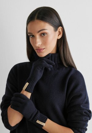 Granatowe rękawiczki z dzianiny z prążkowanymi ściągaczami i metkami z materiału, zestawione z pasującym swetrem z wysokim dekoltem. Miękka faktura, dopasowany krój.