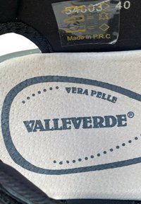 Sottopiede in pelle nera con la scritta "VALLEVERDE" stampata in blu scuro. Sfondo bianco testurizzato con l'etichetta "VERA PELLE" e simboli di cura in oro.