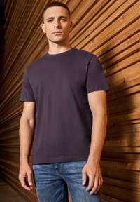 Camiseta de algodón azul marino con mangas cortas, cuello redondo y una textura suave, combinada con jeans de mezclilla sobre un fondo de madera.