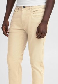 Pantaloni in cotone beige con vestibilità slim, caratterizzati da un classico design a cinque tasche, chiusura con bottone e dettagli di cucitura a vista.