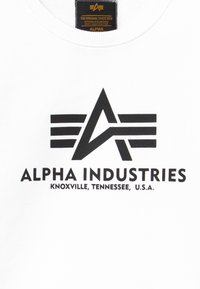 Sweatshirt blanc avec un grand design graphique noir comportant un "A" et des rayures, ainsi que le texte "ALPHA INDUSTRIES KNOXVILLE, TENNESSEE, É.-U."