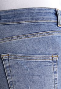 Ljusblå denimjeans med en strukturerad yta, som har två bakfickor och synliga sömmar. Något slitna detaljer på tyget.