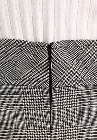 Černobílá vzorovaná látka se zipovým uzávěrem na zadní straně. Design obsahuje kombinaci vzoru houndstooth a kostkovaného vzoru.