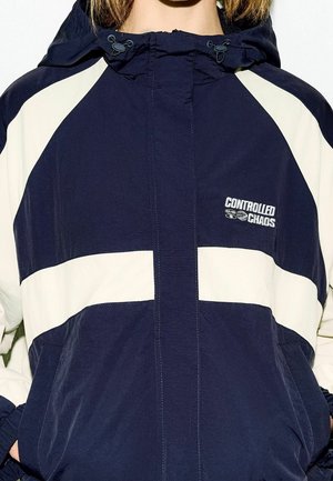 Námořnický větrovka s krémovými pruhy, s kapucí, s elastickým lemem a manžetami. Logo značky "Controlled Chaos" na hrudi. Lehká tkanina.