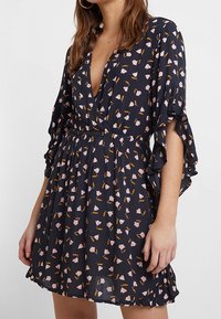 Marinblå klänning med korta volangärmar, djup V-ringning och elastisk midja. Drags till med rosa blommönster och en utsvängd kjol. Lättviktigt material.