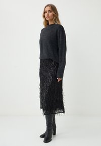 Maglione lavorato a maglia grigio scuro con colletto alto e maniche lunghe, abbinato a una gonna nera con frange di paillettes e stivali neri con tacco al ginocchio.