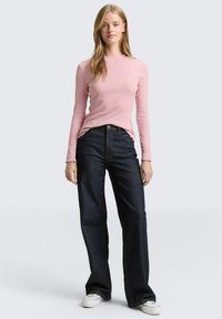Pink ribbed long-sleeve top paired with dark blue wide-leg jeans, featuring a button closure and white sneakers. Smooth textures and clean design.