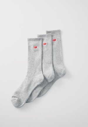 Graue Baumwollsocken mit gerippter Textur, verziert mit roten New Balance-Logos. Drei Paar zur Präsentation ausgerichtet.