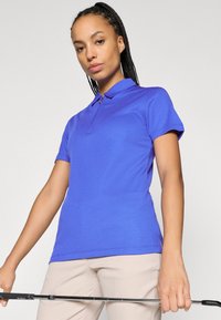 Īsām piedurkņu, ar apkakli polo krekls dzīvīgā zilā krāsā ar teksturētu audumu. Ar rāvējslēdzēja atvēršanu un sporta biksēm, rokā tur kārti golfu.