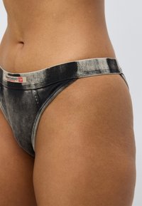 Graue Tanga-Unterwäsche im Denim-Stil mit einem verblassten schwarzen Design, ausgestattet mit einem weichen, breiten beigen Bund. Glatte Textur mit dezenten Nahtdetails.