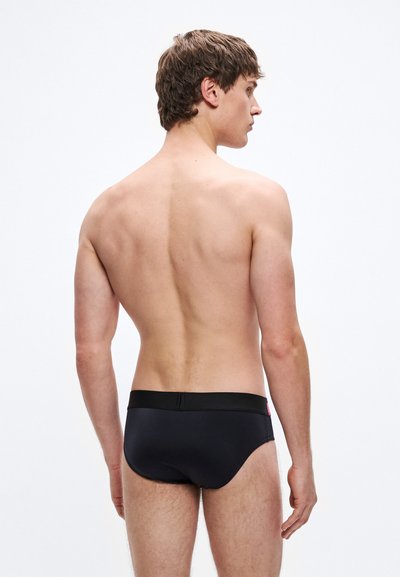 Mustad ujumispüksid paksu musta vöökohaga, millel on minimalistlik disain. Sile tekstuur ja vormitud kujundus, sobilik ujumiseks.