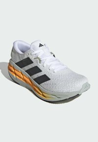 White athletic shoe with grey accents, featuring a textured upper, three black stripes, and an orange and grey sole. Laced design, light padding.