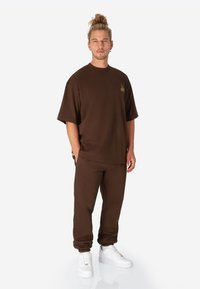 Bruin katoenen oversized T-shirt met korte mouwen en kleine plantenafbeelding, gecombineerd met bijpassende joggers en witte sneakers.