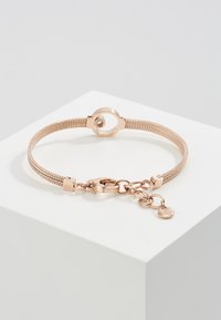 Bracelet en maille dorée rose avec un fermoir circulaire, présentant une surface texturée et une chaîne ajustable avec un charm pendentif.