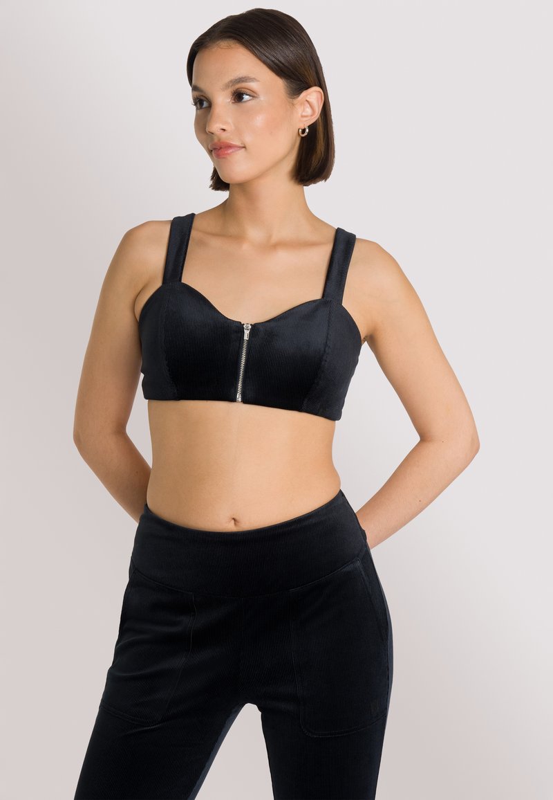 Top corto in corduroy nero con spalline larghe e dettaglio con zip frontale, abbinato a pantaloni in corduroy nero a vita alta. Texture liscia.