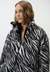 Zwart-witte zebra gestreepte nepbont jas met hoge kraag en ritssluiting aan de voorkant, met een pluche textuur en een ontspannen pasvorm.