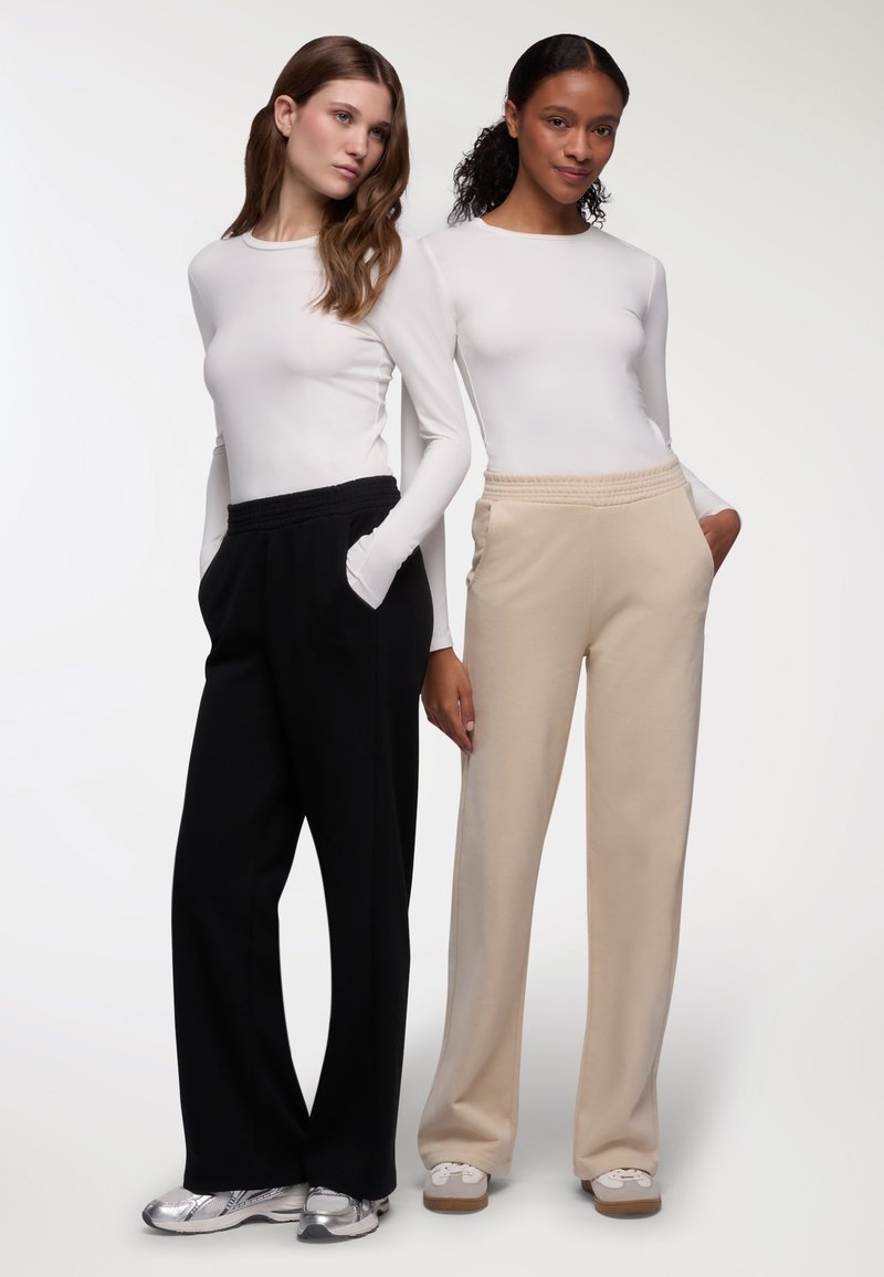 Due magliette a manica lunga bianche abbinate a pantaloni a gamba larga: uno nero e uno beige. I pantaloni presentano una vita elasticizzata e tasche laterali.