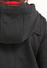 Cappotto nero con cappuccio in un tessuto testurizzato, con una fodera a quadri rossi e neri visibile al colletto. Design del cappuccio spesso e strutturato.