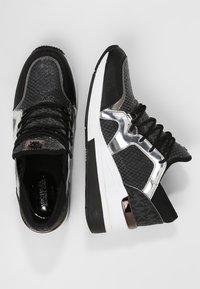 Zapatillas negras y grises con suelas blancas, detalles metálicos plateados, cordones negros y parte superior de tela texturizada, mostradas desde vistas superior y lateral.