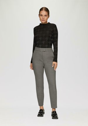 Zwarte lange mouw top met een hounds-tooth patroon, gecombineerd met grijze op maat gemaakte broeken. Schoenen zijn zwarte glanzende instappers.