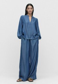 Blå denimtröja med en grund V-ringning och vida ärmar, tillsammans med matchande löst sittande byxor, med en mjuk textur och avslappnad stil.