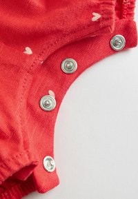 Piros pamut body apró fehér szívmintákkal, fém patenttal az oldalán, puha, texturált anyagból.