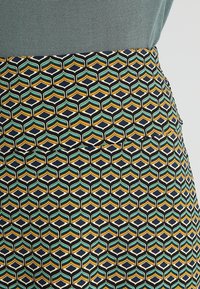 Jupe à motifs présentant un design géométrique avec des teintes turquoise, jaune et marine ; fabriquée en tissu texturé avec une silhouette ajustée.