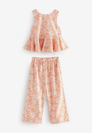 Peplum-top og brede bukser sæt i koralfarve med hvidt blomstermønster. Toppen har en rund halsudskæring og knapdetalje bagpå; bukserne har en elastisk talje.