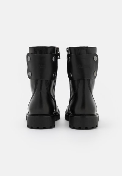 Black leather ankle boots featuring side zippers, round toe, thick rubber sole, and decorative leather straps with metal snaps.