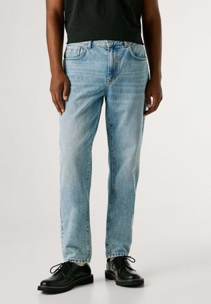 Vaqueros de mezclilla azul claro con corte recto, que cuentan con bolsillos delanteros y traseros y un acabado desgastado. Combinados con zapatos negros de cordones.