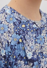 Tessuto di cotone floreale con uno sfondo blu scuro, caratterizzato da diverse tonalità di fiori blu e gialli in vari motivi e texture.