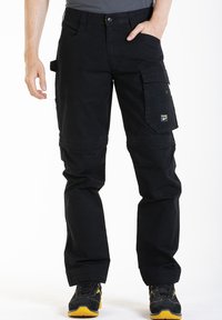 Pantalons cargo noirs en tissu résistant, avec plusieurs poches, une coupe ample et des coutures renforcées. Associés à des chaussures noires et jaunes.