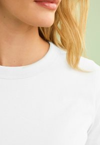 White cotton t-shirt with a round neck, smooth texture, and short sleeves. Simple design, no visible logos or patterns.