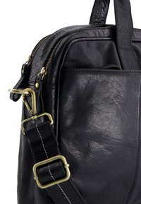 Černá kožená taška přes rameno s mosaznou sponou a zipovými detaily, která má prošívaný nastavitelný popruh a přední kapsu.