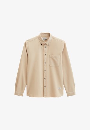 Beiges, langärmliges Hemd zum Knöpfen mit Brusttasche vorne und schwarzen Knöpfen, mit einem kleinen Etikett nahe dem Saum.