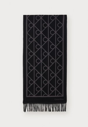 Écharpe noire avec un motif géométrique gris, ornée de bords frangés. Le matériau semble doux et texturé. Le logo de la marque est visible dans le coin.